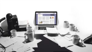 Een rommelig bureau met een open laptop en papieren.